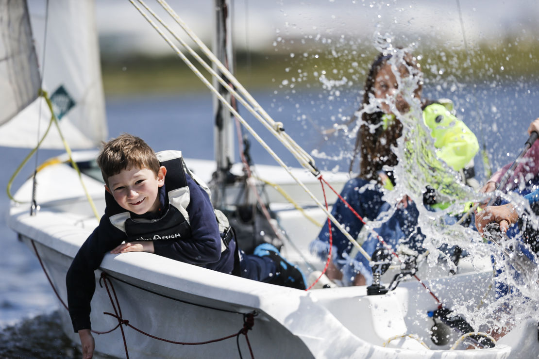 a group of children splashing water while sailing a dinghy