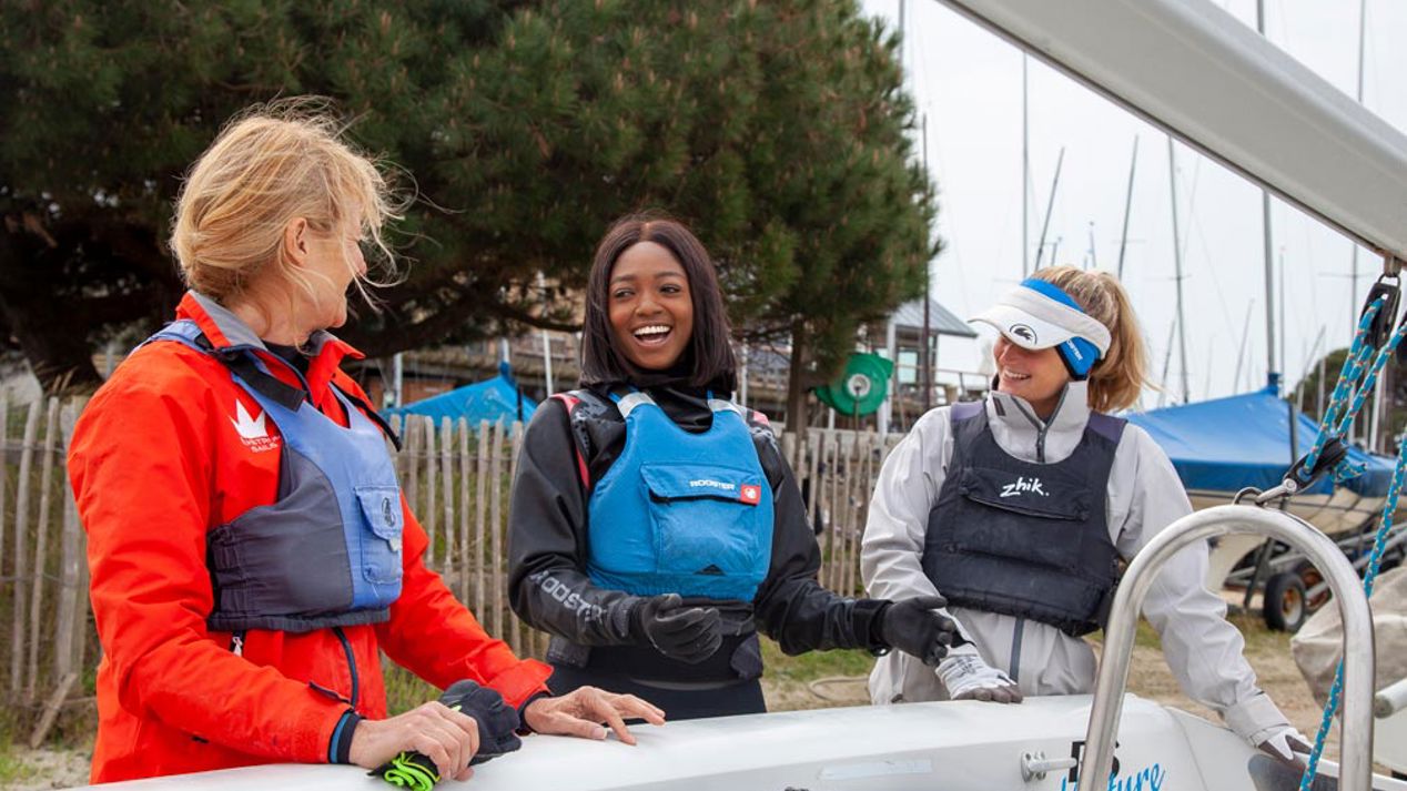 Wide shot of three women stood next to dinghy