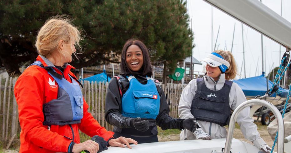 Wide shot of three women stood next to dinghy