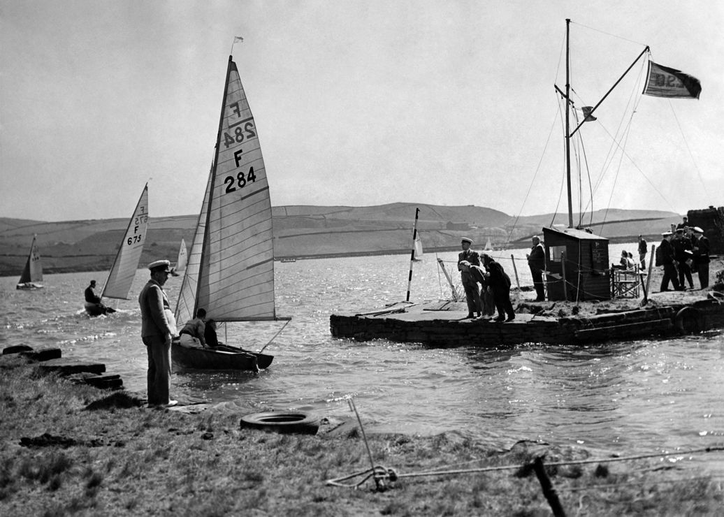 Black and white image of sailors stood on the shore looking out at the water
