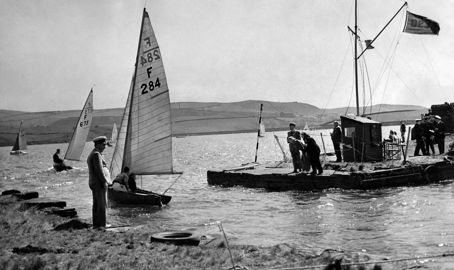 Black and white image of sailors stood on the shore looking out at the water