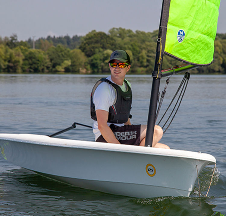 Man on his own sailing in a dinghy wearing sunglasses.