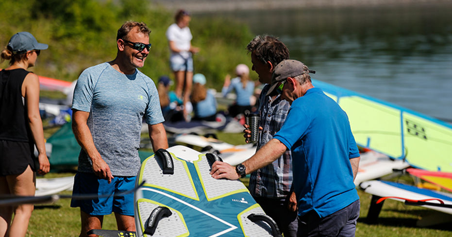 3 men standing around paddle board talking