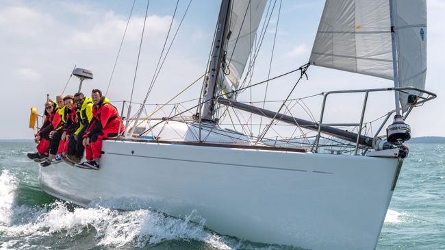 Long shot of crew sat on edge of sailing yacht smiling