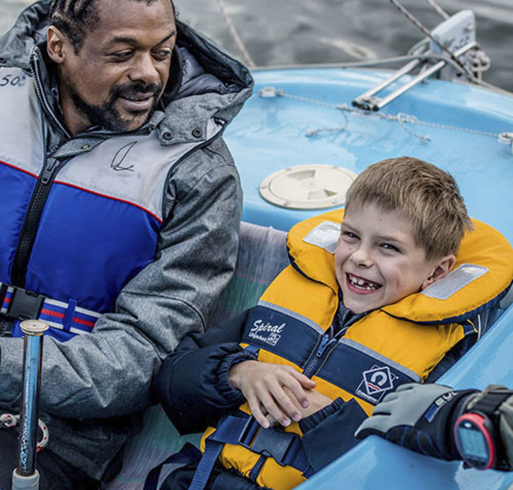 man and a child sailing a dinghy, man is looking at the child, and the child is smiling and looks excited