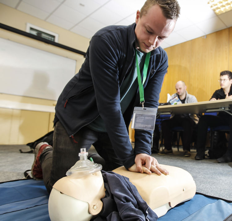 Numerous people in a classroom at a First aid course, one man in knelt on the floor demonstrating CPR on a dummy