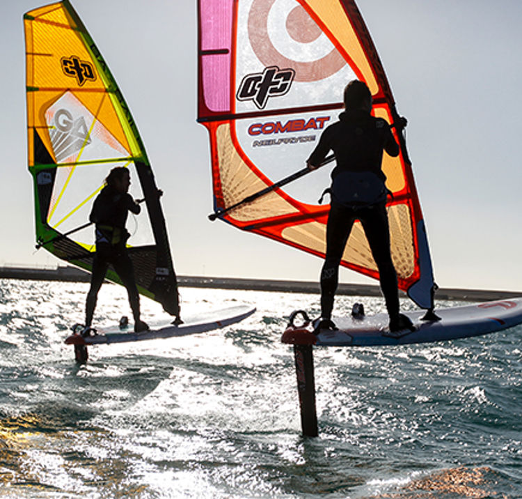 a silhouette of two foiling windsurfers against the sun and sea
