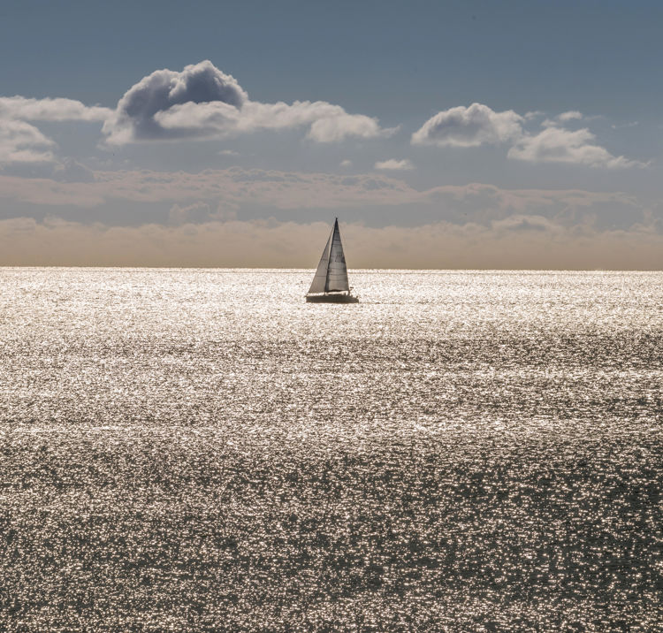 A single boat floating along the horizon at sunset