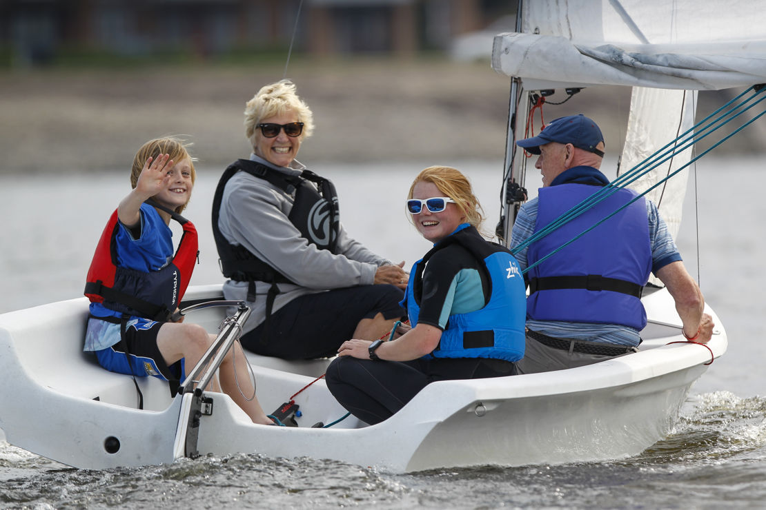 Mid shot of family sailing on a dinghy and smiling at camera