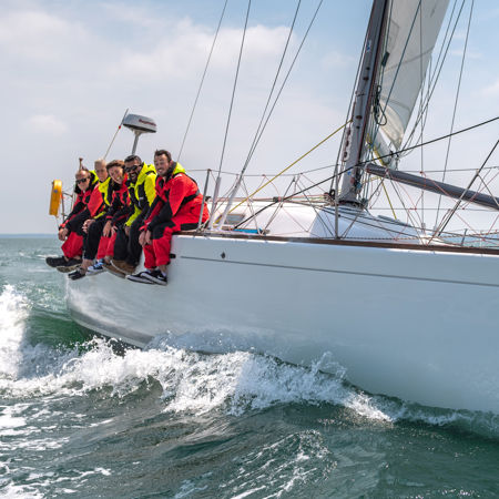 numerous people sat over the side of a sailing yacht whilst sailing on the ocean