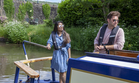 Young couple steering a narrowboat in summer