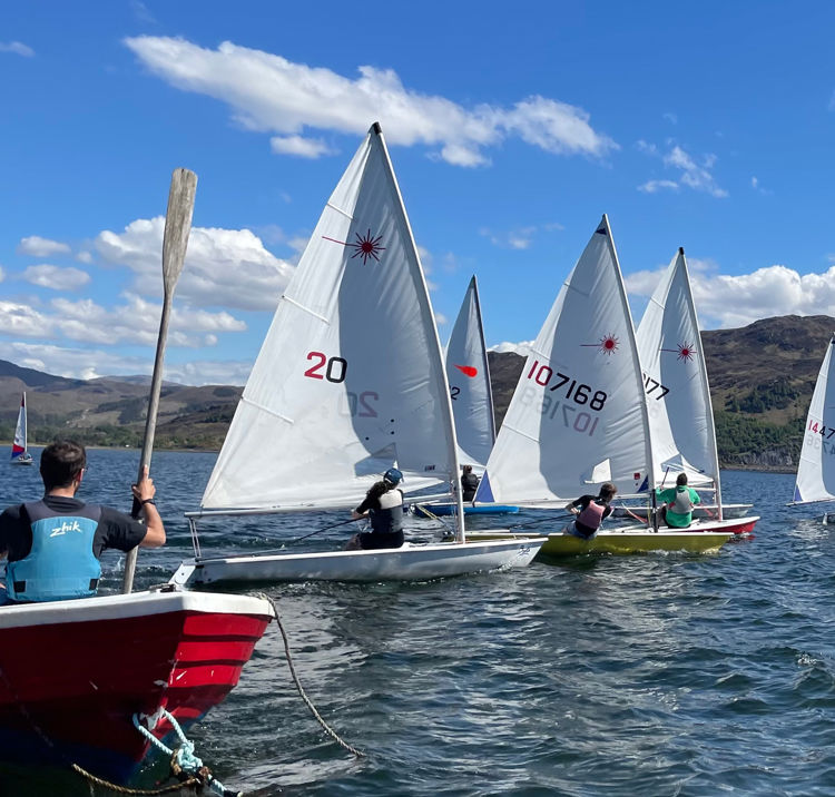 Long shot of five sailing boats with hills in the background