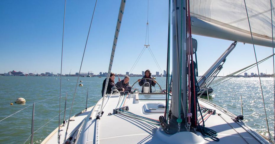 close up of mast cables on board sailing boat, with people in the background and lady steering