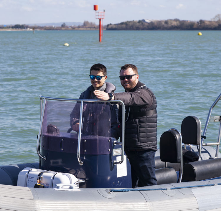 Two men standing on a powerboat, the younger man is steering and older ma is instructing