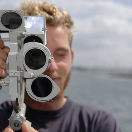close up of man holding a sextant in front of his face