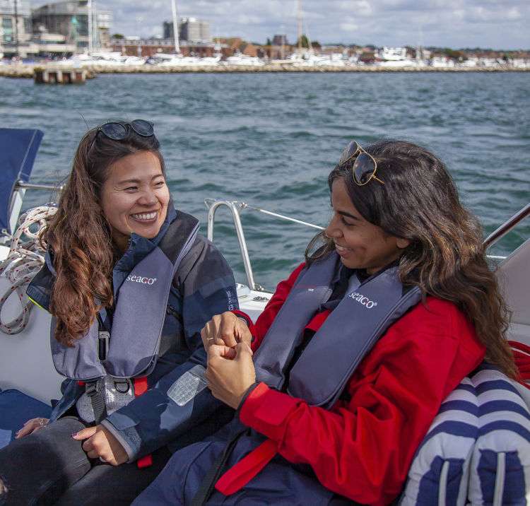 two women sat together on a yacht talking and smiling