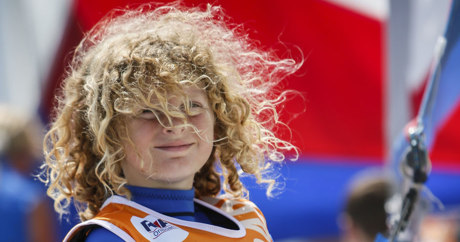 young child with curly hair holding on to ropes. He is wearing an onboard lifejacket