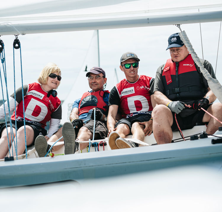 Sailors smiling as they sit over the edge of their boat 