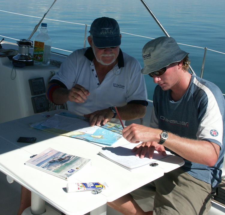 two men sat onboard a yacht, at a table looking at charts and planning