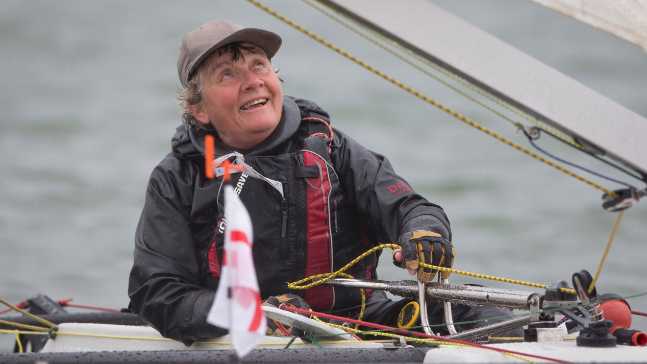 Woman sailing independently, looking up at sail and smiling
