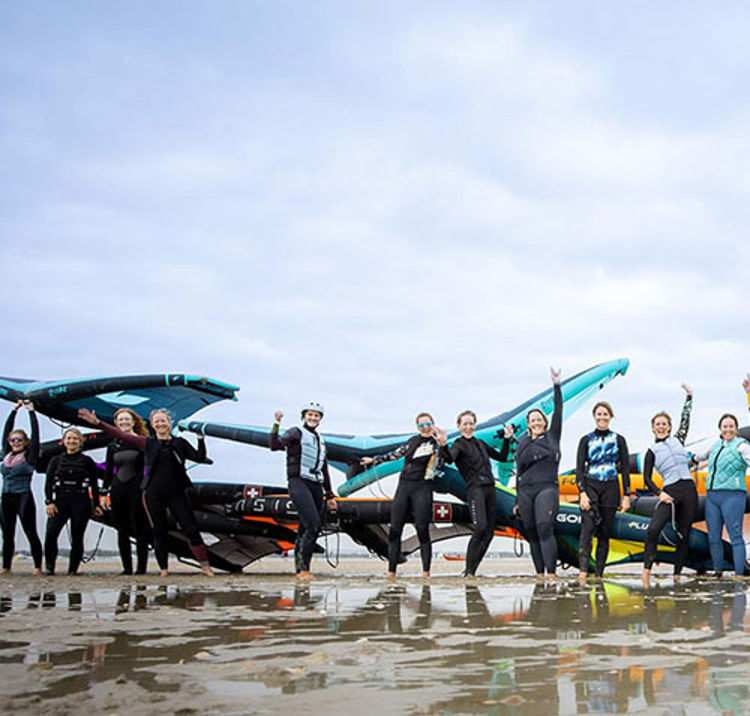 a group of wing surfing women cheering on a beach