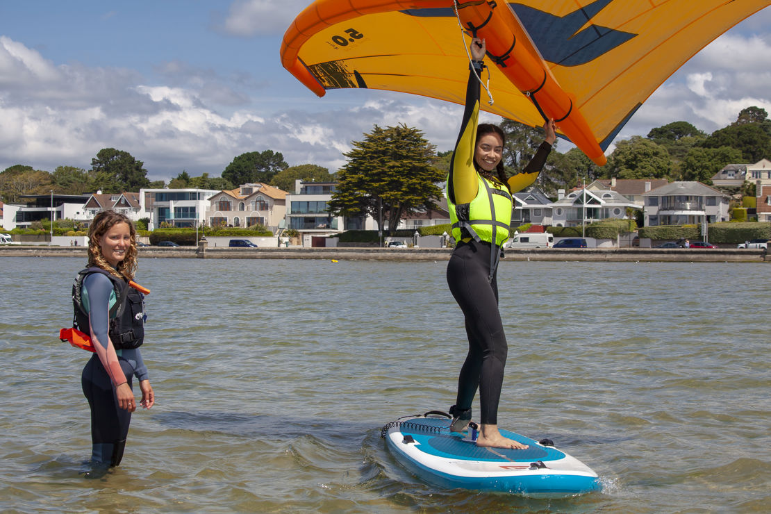 Woman learning to wingsurf, she is on the board, and instructor is in the water