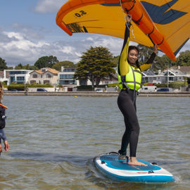 Woman learning to wingsurf, she is on the board, and instructor is in the water