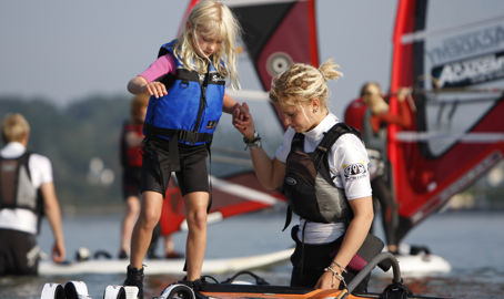 Instructor helping young girl onto windsurfing board