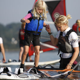 Instructor helping young girl onto windsurfing board