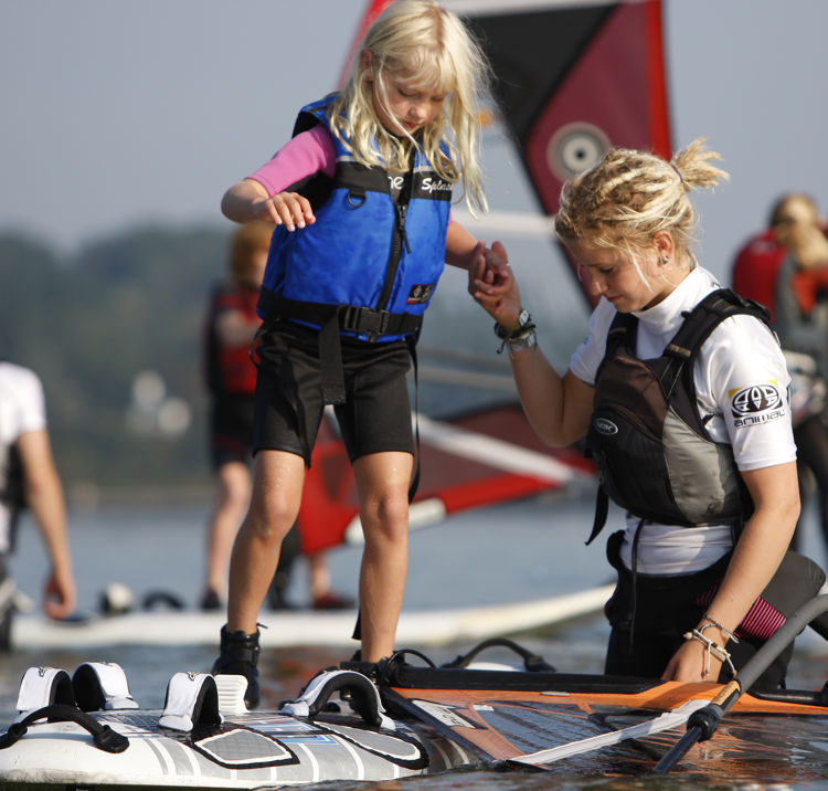 Instructor helping young girl onto windsurfing board